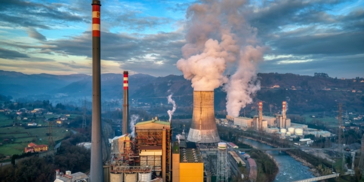 Planta industrial emitiendo humo en un paisaje rural