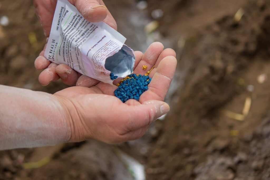 Mano sosteniendo fertilizantes de colores azul y amarillo