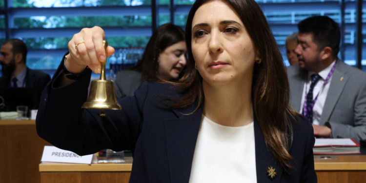 Ministra sosteniendo una campana durante la reunión del Consejo de Asuntos Generales