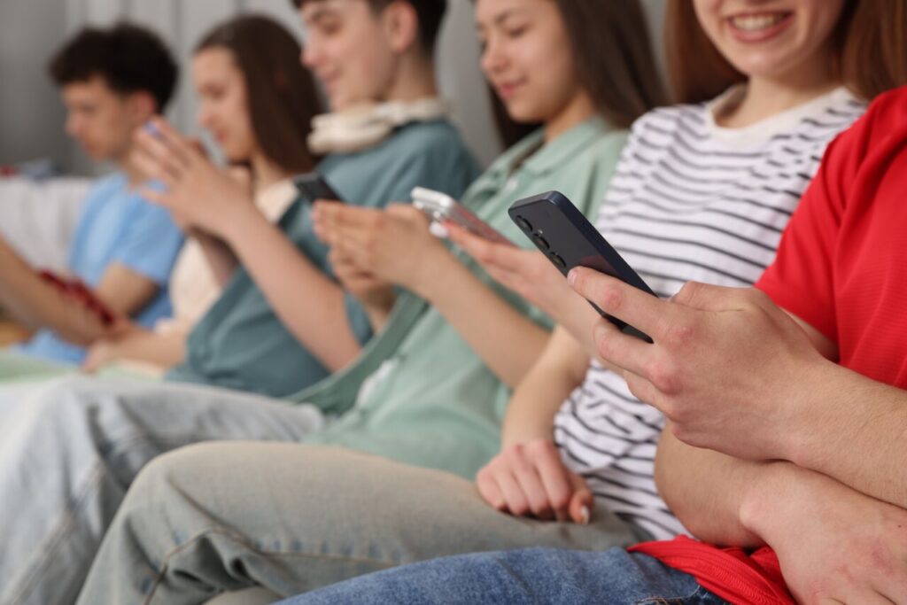 Grupo de adolescentes sentados usando smartphones en un entorno social.