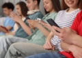 Grupo de adolescentes sentados usando smartphones en un entorno social.
