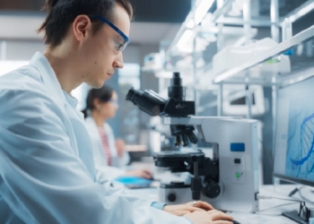 Científico en laboratorio analizando datos con microscopio y computadora