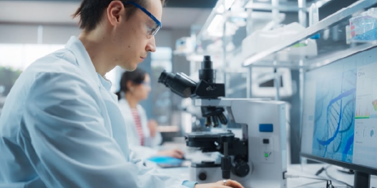 Científico en laboratorio analizando datos con microscopio y computadora