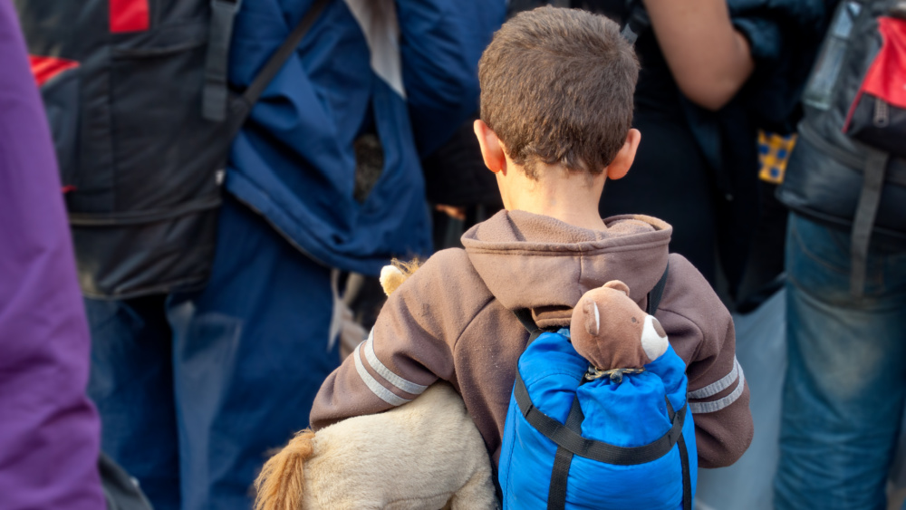 Niño refugiado con mochila y peluche en un entorno de crisis